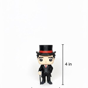 Puede incluir: Figura de un hombre con traje negro, corbata roja y sombrero de copa con una banda roja. La figura mide unos 10 cm de alto y 5 cm de ancho. La figura sostiene un bast&oacute;n. Es un objeto de colecci&oacute;n.