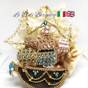 以下が含まれることがあります： ピンク、ブルー、グリーンのビーズが付いたゴールドビーズの船のペンダント。船はゴールドチェーンで飾られており、ブラウンフェルトのベースが付いています。