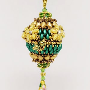 Può includere: Una collana con catena dorata con un ciondolo di perline verdi e dorate. Il ciondolo è una sfera con una perla a forma di lacrima che pende dalla parte inferiore. La perla a forma di lacrima è verde con un motivo a fiore bianco.