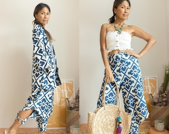 May include: Two women wearing blue and white patterned pants. One woman is wearing a white strapless top and a gold necklace. The other woman is wearing a blue and white patterned jacket. Both women are holding a straw bag.