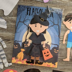 May include: A paper craft Halloween witch doll with a black dress, black hat, and orange and black striped stockings. The witch is holding a small orange pumpkin-shaped bag. The background is a dark blue sky with a full moon and trees.