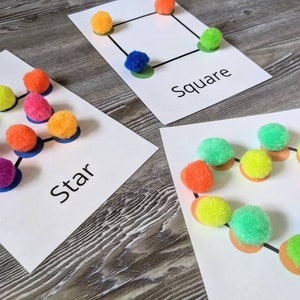 May include: Three white cards with different shapes drawn on them. Each shape has colorful pom-poms placed on the dots. The cards are labeled "Star", "Square", and "Circle".