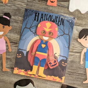 May include: A Halloween-themed paper craft set with a red, blue, and yellow superhero character holding a jack-o'-lantern. The set also includes a girl with brown hair, a boy with brown hair, and a ghost.