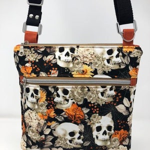 May include: A black and orange fabric crossbody bag with a skull and floral print. The bag has a zipper closure and an adjustable strap.