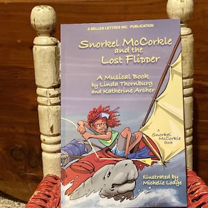 Könnte beinhalten: Ein Kinderbuch mit dem Titel "Snorkel McCorkle and the Lost Flipper" wird gezeigt. Das Cover zeigt eine Illustration einer Person, die auf einem roten Meeresbewohner segelt. Das Buch ist ein Musikbuch von Linda Thornburg und Katherine Archer.