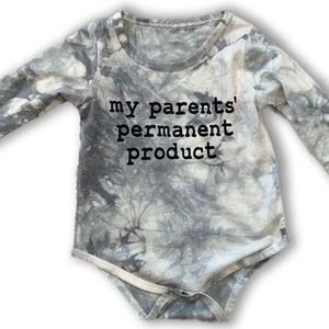 May include: A grey and white tie-dye long-sleeved baby onesie with the text "my parents' permanent product" in black.