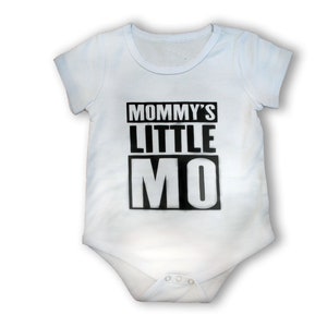 May include: A white baby onesie with black text that reads "Mommy's Little Mo".