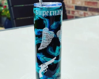 May include: A black and blue stainless steel tumbler with a white design of angel wings and a gun. The tumbler has the text "Supernatural" and "Drive Shotgun" on it.