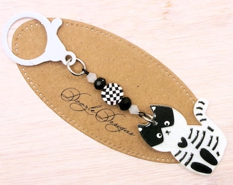 May include: Black and white cat charm keychain with a checkerboard bead and black beads. The charm is attached to a silver key ring.