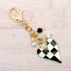 May include: A gold-colored charm with a heart-shaped pendant featuring a black and white checkered pattern. The charm includes a lobster clasp, small beads, and a chain. The heart pendant is approximately 1.5 inches long.