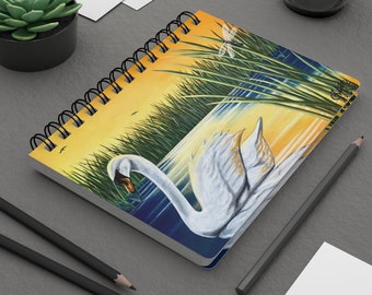 May include: A spiral bound notebook with a white swan swimming in a blue lake with yellow and green reeds in the background. The cover features a dragonfly.