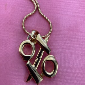 May include: A gold chain necklace with a pendant shaped like the percentage symbol. The pendant is made of two interlocking circles with a line through the center.