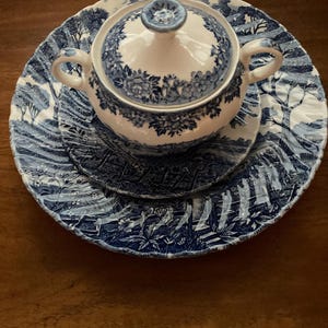 May include: A blue and white porcelain sugar bowl and lid with a floral design. The bowl is sitting on a matching saucer.