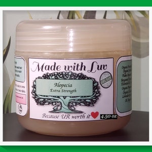 Puede incluir: Un tarro de pl&aacute;stico transparente con una etiqueta marr&oacute;n claro que dice "Made with Luv Alopecia Extra Strength Because UR worth it 4.50 oz". La etiqueta tambi&eacute;n presenta un &aacute;rbol verde con un coraz&oacute;n y la palabra "ORGANIC" en un c&iacute;rculo.