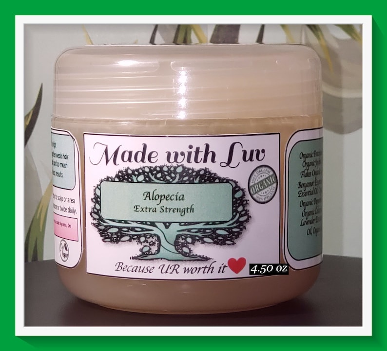 Puede incluir: Un tarro de pl&aacute;stico transparente con una etiqueta marr&oacute;n claro que dice "Made with Luv Alopecia Extra Strength Because UR worth it 4.50 oz". La etiqueta tambi&eacute;n presenta un &aacute;rbol verde con un coraz&oacute;n y la palabra "ORGANIC" en un c&iacute;rculo.
