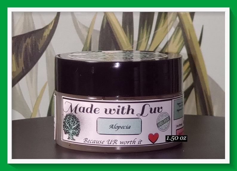 Puede incluir: Un peque&ntilde;o tarro marr&oacute;n con tapa negra. La etiqueta dice "Made with Luv" con un logotipo de &aacute;rbol, "Alopecia", "Because U'R worth it" y un coraz&oacute;n rojo. El tarro tambi&eacute;n tiene una etiqueta "Organic" y dice "1.50 oz".