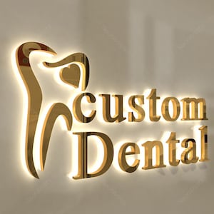 Op de afbeelding: Gouden gepersonaliseerd tandartsbord met een gestileerde tand en de woorden "custom dental" in reliëfletters.