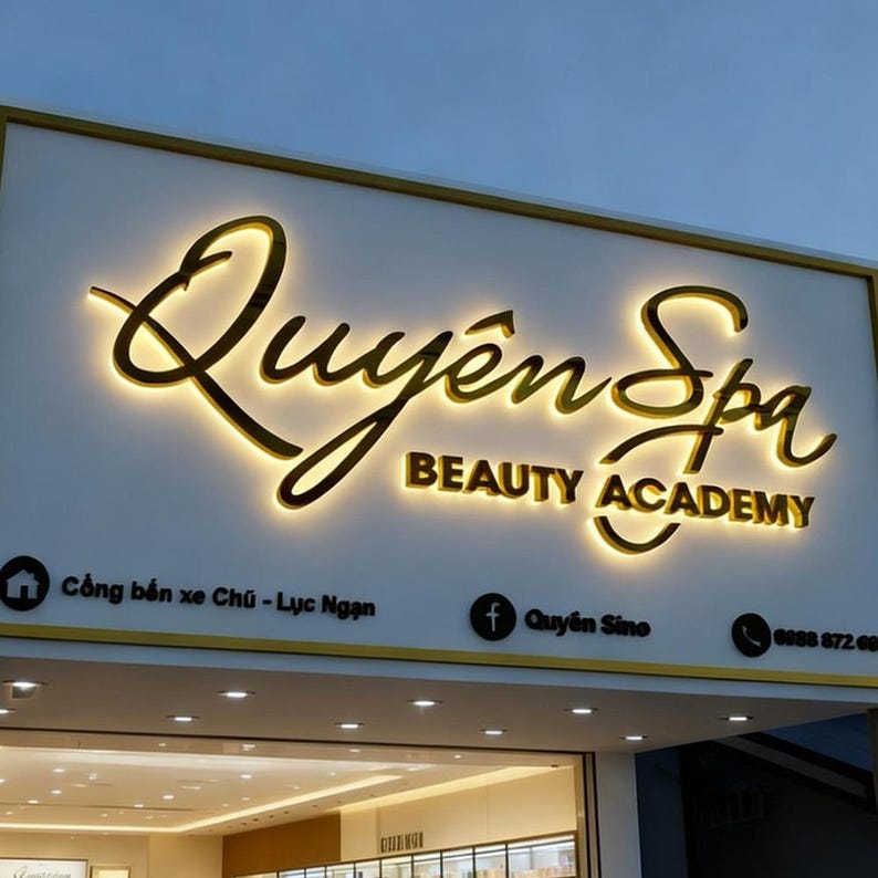 May include: Illuminated sign for Quy&ecirc;n Spa Beauty Academy. The sign features gold lettering against a white background. The text includes the business name and the words "BEAUTY ACADEMY". Additional text and contact information are also visible.