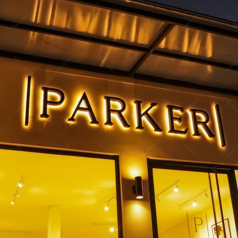 May include: A storefront sign with the name "PARKER" in illuminated, dark letters. The sign is mounted on a beige wall above a large window. The lighting creates a warm, inviting atmosphere.