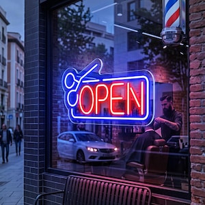 May include: A neon sign in a storefront window displays the word OPEN in red letters surrounded by a blue rectangular border and a blue scissor icon. A traditional red, white, and blue barber pole is mounted on the exterior brick wall above.