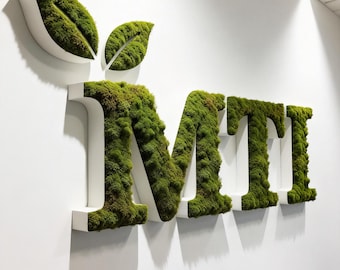 May include: White wall art featuring the letters "MTI" covered in green moss, with two white leaf-shaped accents. The letters are large and three-dimensional, creating a striking visual effect. The moss adds a natural, textured element to the design.