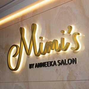 May include: A wall-mounted sign for "Mimi's" salon. The gold-colored, illuminated letters are in a cursive font. Below, the text "BY ANNEEKA SALON" is in black, sans-serif font. The background is a light-colored, textured wall.
