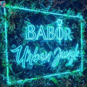 May include: A rectangular neon sign with bright blue light emitting the text BABOR and Urban Jungle, featuring a stylized rose icon above the text, all mounted against a dense background of various green artificial tropical leaves.