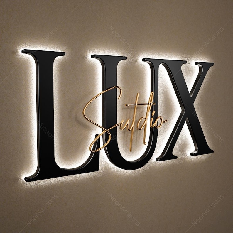 May include: A black illuminated sign that reads "LUX Studio" in a modern font. The letters "LUX" are large and bold, with a glowing white outline. The word "Studio" is in a cursive gold font, centered within the "U".