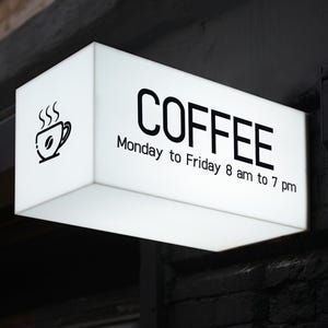 May include: White rectangular sign with black text that reads "COFFEE" and "Monday to Friday 8 am to 7 pm". A small black and white icon of a coffee cup with steam is in the top left corner.