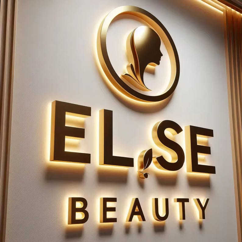 May include: A gold-colored illuminated sign for "ELSE BEAUTY" on a white wall. The sign features a circular emblem with a woman's profile and the brand name in bold, block letters. The word "BEAUTY" is also illuminated.