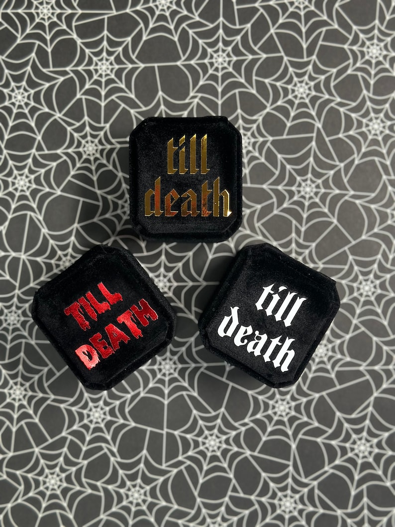 K&ouml;nnte beinhalten: Drei schwarze Samt-Ringboxen mit unterschiedlichfarbiger Beschriftung. Die Boxen sagen "till death" in goldener, roter und wei&szlig;er Schrift.