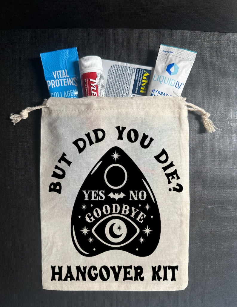 May include: A white canvas bag with a black design of a Ouija board with the text "But did you die?" and "Hangover Kit". The bag contains various items, including a blue packet of Vital Proteins Collagen, a red tube of Tylenol, a white packet of Advil, and a blue packet of Liquid IV.
