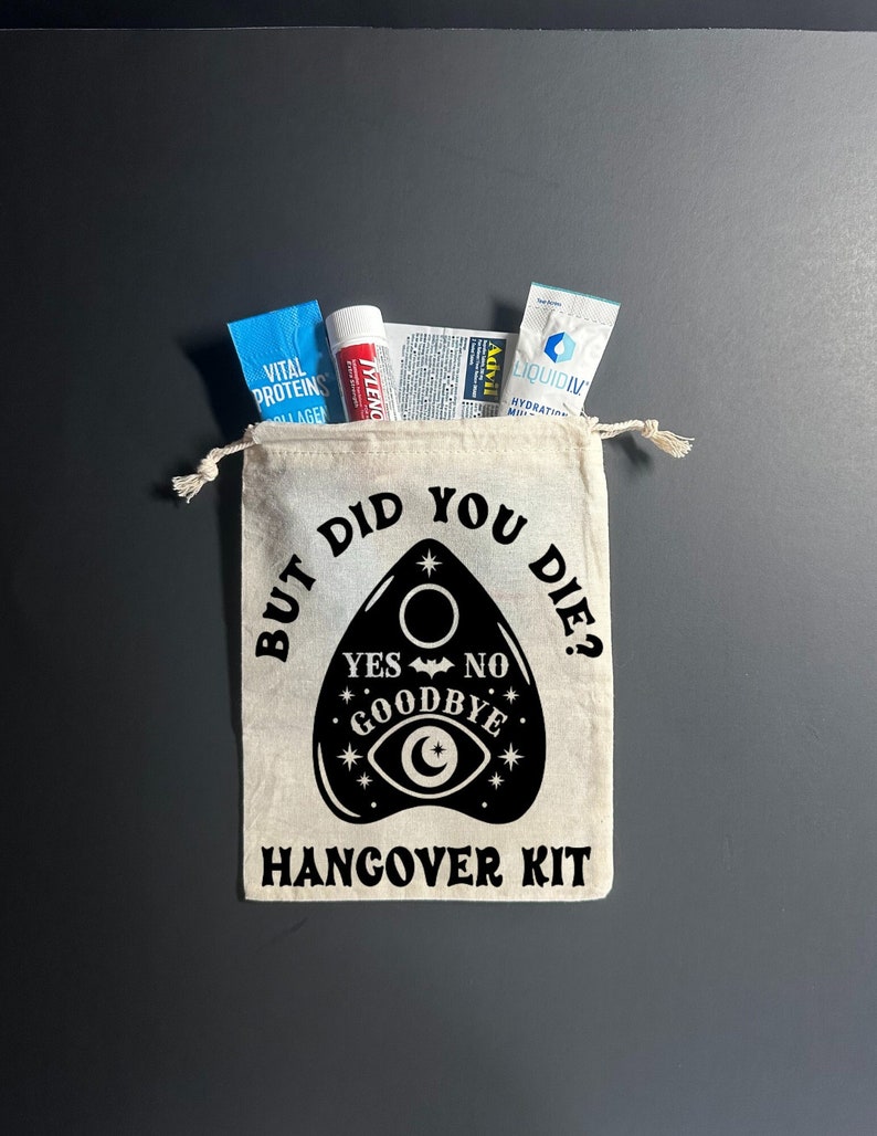 May include: A white canvas bag with a black design of a Ouija board with the text "But did you die?" and "Hangover Kit". The bag contains various items, including a blue packet of Vital Proteins Collagen, a blue packet of Liquid IV Hydration Multiplier, a white tube of Tylenol, and a white packet of Advil.