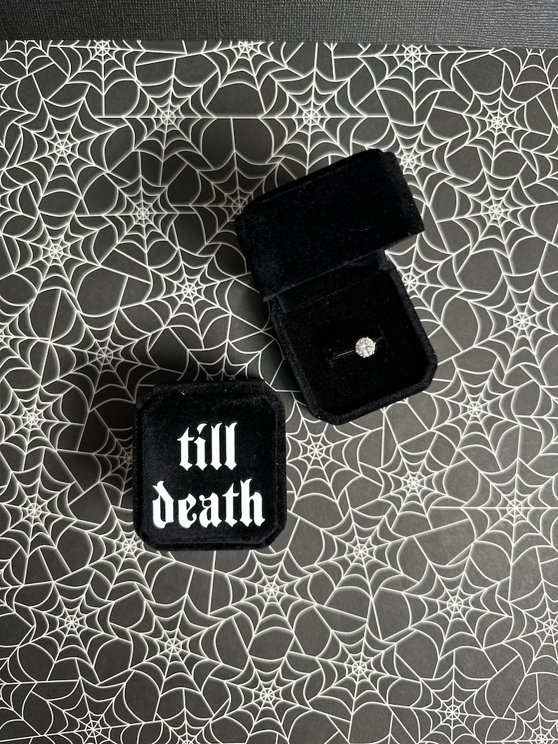 K&ouml;nnte beinhalten: Schwarze Samt-Ringbox mit den Worten "till death" in wei&szlig;en gotischen Buchstaben. Die Box ist ge&ouml;ffnet und ein Diamantring befindet sich darin.