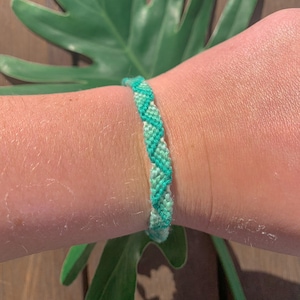 May include: A green and white friendship bracelet with a chevron pattern.