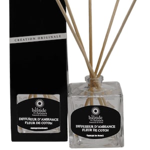 Peut inclure: Un flacon en verre transparent avec un bouchon noir et des bâtonnets en bois. L'étiquette est noire et blanche avec le texte "bastide" et "Diffuseur d'ambiance Fleur de Coton". Le flacon est posé sur une surface blanche. Le texte "Fabrication artisanale" est sur une boîte noire derrière le flacon.