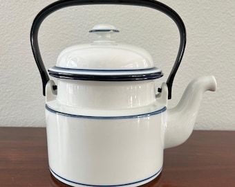 May include: White porcelain teapot with a black handle and blue trim. The teapot has a lid and a spout.