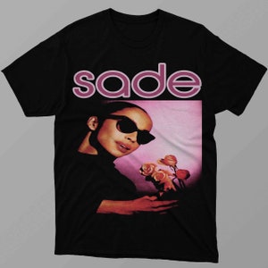Könnte beinhalten: Schwarzes T-Shirt mit einem pinkfarbenen "Sade"-Motiv und einem Foto von Sade mit Blumen.
