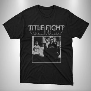 Może przedstawiać: Czarny t-shirt z białym napisem "TITLE FIGHT" nad czarno-białym zdjęciem zespołu. Członkowie zespołu noszą codzienne ubrania.