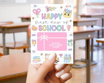 May include: A pink gift card featuring the text "HAPPY first day of SCHOOL" and school-themed illustrations. The card includes a pink gift box graphic with the text "PLACE GIFT CARD HERE". The card is held in a person's hand.