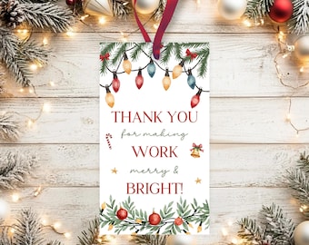 May include: A white rectangular gift tag with a red ribbon. The tag features a watercolor design of Christmas lights, greenery, and ornaments. Text on the tag reads "THANK YOU for making WORK merry & BRIGHT!" A festive holiday-themed gift tag.