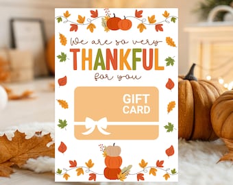 May include: Thanksgiving-themed gift card with the text "We are so very THANKFUL for you." The card features a light orange background with a white bow and the words "GIFT CARD." Decorative pumpkins and fall leaves surround the card.