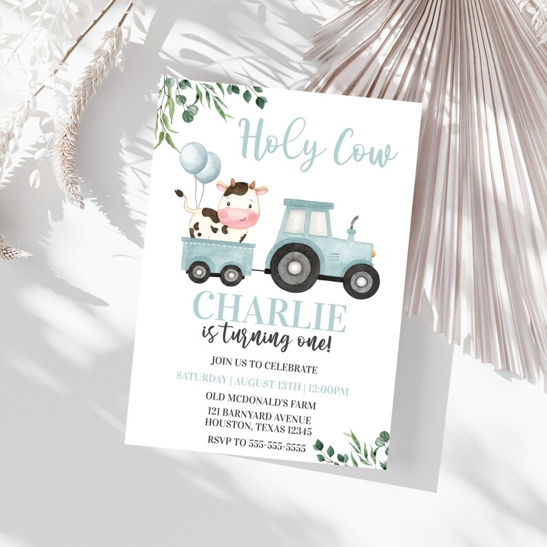 Puede incluir: Una invitaci&oacute;n de cumplea&ntilde;os azul y blanca con una vaca y un tractor de dibujos animados. El texto dice "Holy Cow Charlie is turning one!" con detalles para la fiesta.