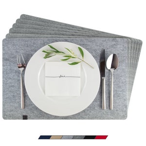 Può includere: Un set di sei tovagliette all'americana in feltro grigio con un piatto bianco, posate e un rametto di verde in cima. Il piatto ha un biglietto bianco con la parola "love" scritta su di esso.