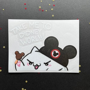 May include: A white sticker with a cartoon cat wearing a black Mickey Mouse hat and holding a brown ice cream bar. The sticker has the text "TAKE ME TO DIDNEY WORL!!!" in white.