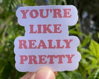 May include: A white die-cut sticker with a wavy, cloud-like border featuring the text "YOU'RE LIKE REALLY PRETTY" printed in a bold, pink, serif font. The sticker has a smooth, matte finish and is shaped to follow the contour of the three lines of text.