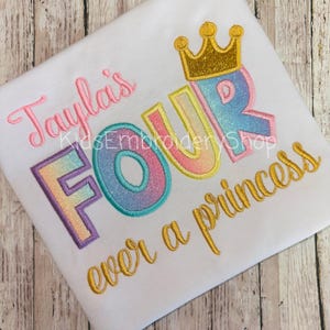 May include: A white t-shirt with the text "Tayla's Four ever a princess" embroidered in gold and rainbow colors. A gold crown is above the word "Four".