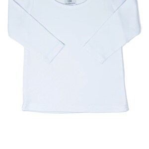 May include: White long-sleeve shirt with a round neckline. The shirt has a small tag with the text "AJ Blanks 12M 100% Combed Cotton" on the front.