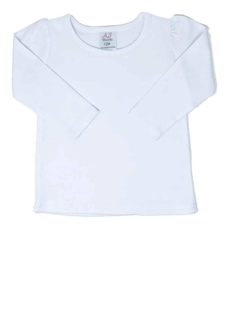 May include: White long-sleeve shirt with a round neckline. The shirt has a small tag with the text "AJ Blanks 12M 100% Combed Cotton" on the front.