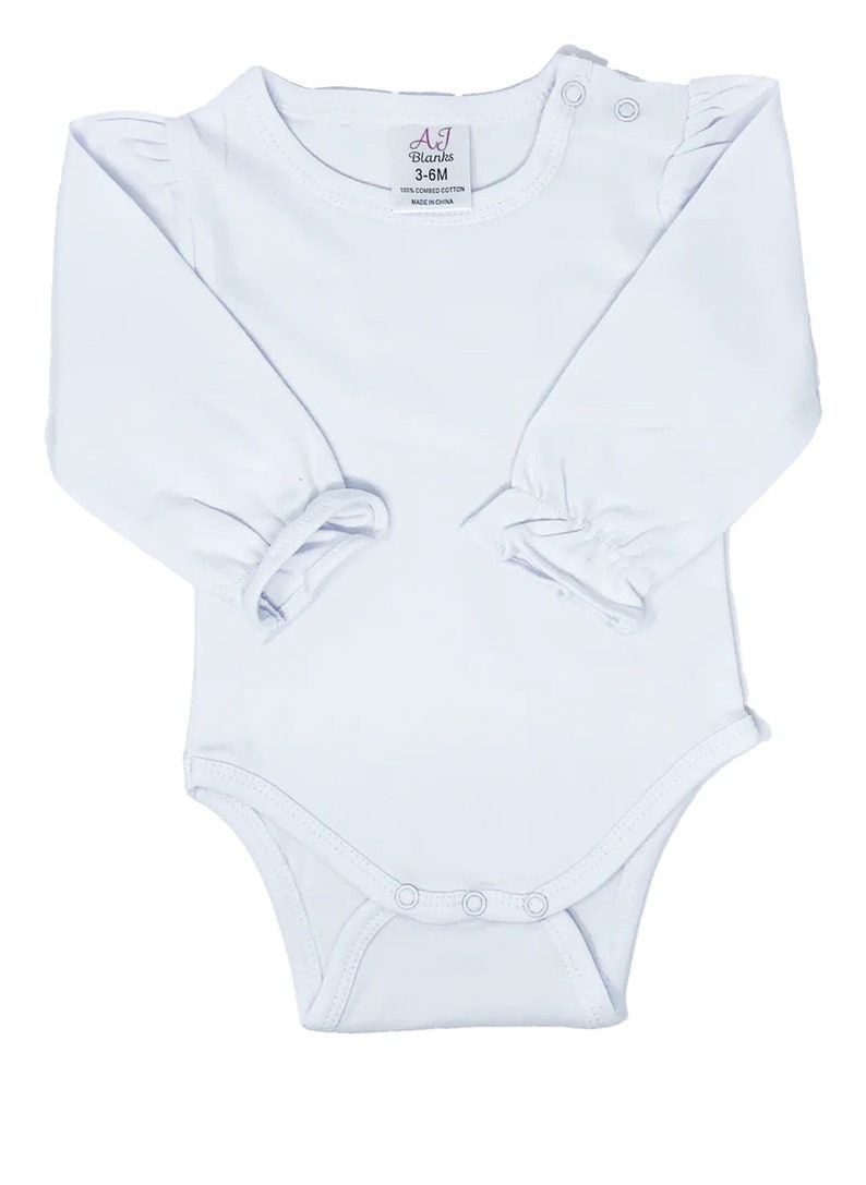 May include: White long-sleeve baby onesie with ruffled sleeves and snap closures. The onesie has a label that reads "AJ Blanks 3-6M 100% Combed Cotton Made in China."